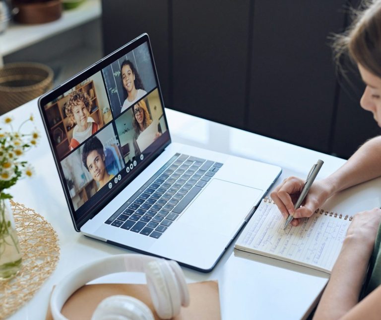 FORMATION & MASTERCLASS Polymathia Group Femme prenant des notes lors d'une réunion en visioconférence sur un ordinateur portable.